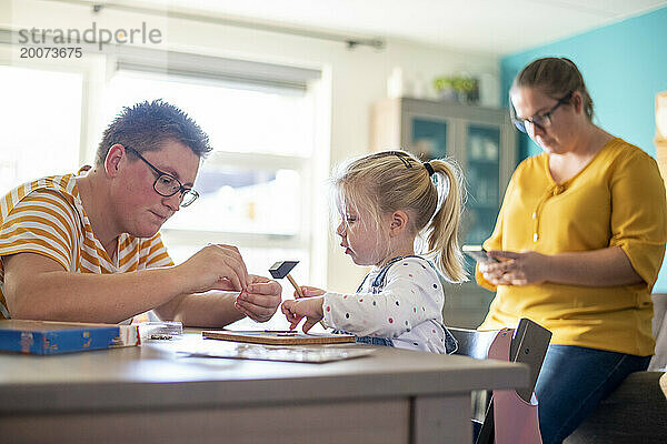 Gleichgeschlechtliche Familie sitzt am Esstisch und spielt gemeinsam Spiele  um eine Bindung zu ihrer Tochter aufzubauen