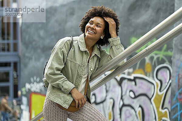 Trendige junge Afrikanerin gemischter Abstammung  die glücklich durch die Stadt läuft. spielt mit ihren Haaren