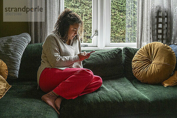 Erwachsene Frau sitzt auf dem Sofa und entspannt sich mit ihrem Telefon