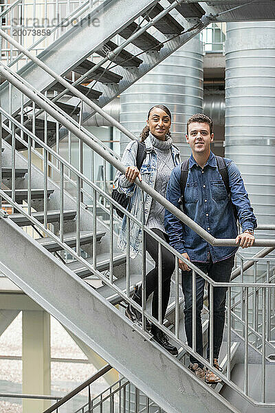 Männliche und weibliche Studenten gemischter Abstammung stehen auf der Treppe ihrer Universität und sehen positiv aus