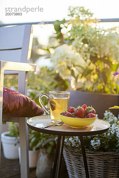 Frühstück mit Tee und Erdbeeren auf einem schönen Tisch in der Sommersonne. Garten und Kräuter in voller Blüte  Blumen.