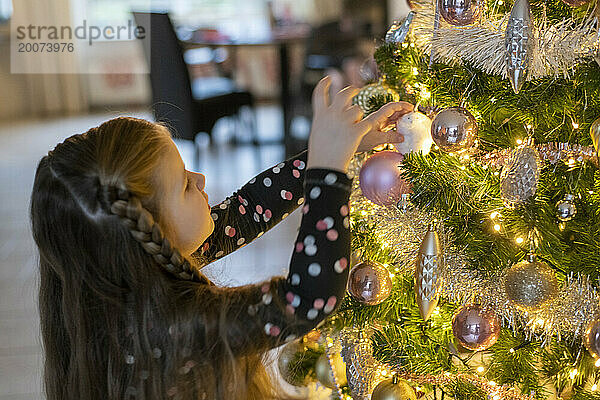 Alleinerziehende Mutter hilft ihren Töchtern  Ornamente an ihrem Baum anzubringen. Ein wunderschöner Moment der Bindung mit funkelnden Lichtern und Kugeln.