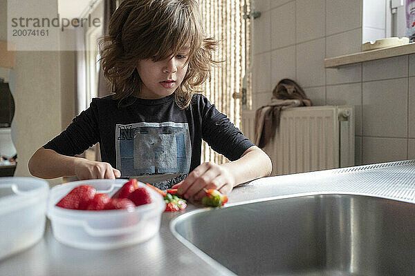 Kleiner Junge schneidet Erdbeeren für sein gesundes Mittagessen