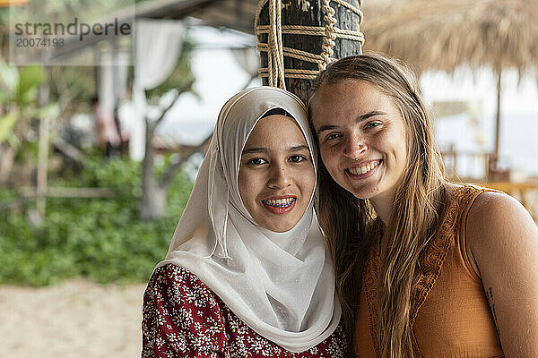 Lächelndes Porträt zweier bester Freundinnen  eine davon trägt einen Hijab in einem Strandresort im Süden Thailands.