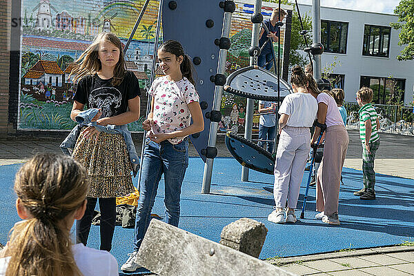 Junge Gruppe von Kindern wird von ihrem Lehrer auf dem Schulhof beaufsichtigt