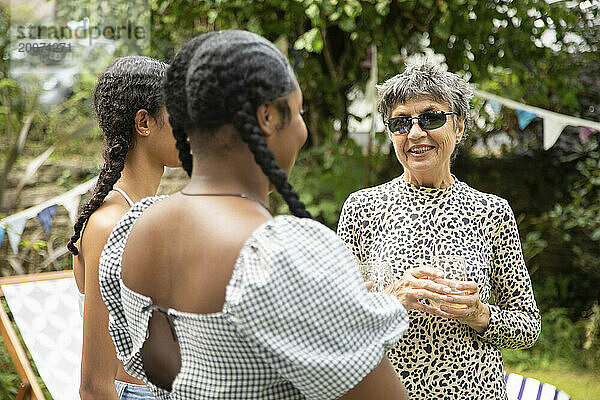 Eine reife weiße Frau plaudert und lacht mit zwei jungen schwarzen Frauen auf einer Gartenparty