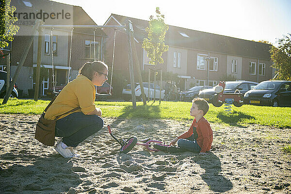 Gleichgeschlechtliche Mutter sitzt mit ihrem Sohn im Park. Kleiner Junge spielt im Sandkasten  während seine Mutter Freundschaft mit ihm knüpft und glückliche Momente mit ihm genießt