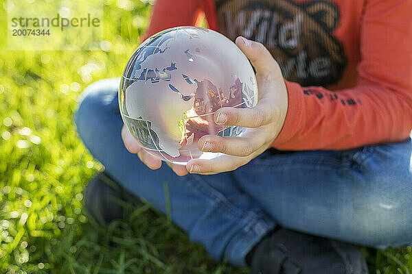 Kind hält eine Glaskugel in einem öffentlichen Park  reflektierendes Licht und klares Glas