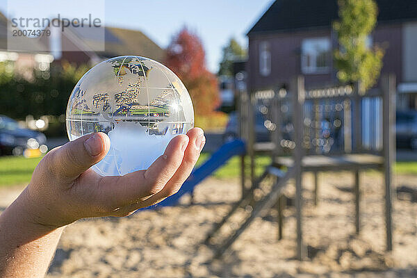 Kind hält eine Glaskugel in einem öffentlichen Park  reflektierendes Licht und klares Glas