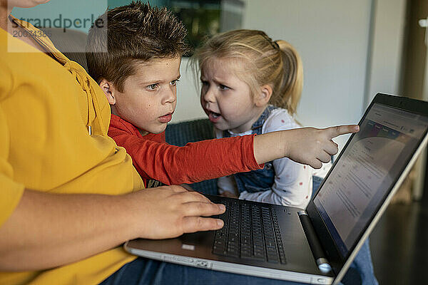 Mutter sitzt mit ihrem Sohn und ihrer Tochter zusammen und unterrichtet ihn am Laptop