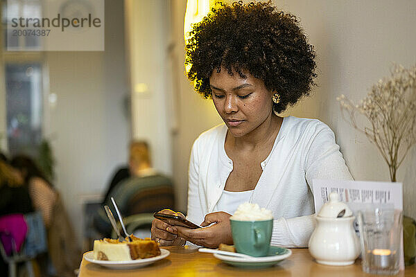Attraktive Afrikanerin mit schönen Haaren sitzt mit ihrem Telefon in einem Café