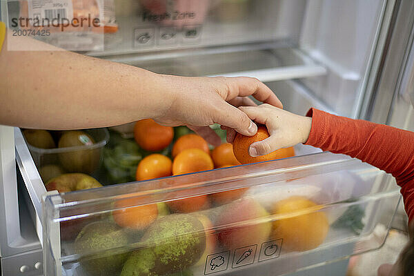 Mother giving her son a healthy snack  fruit from the fridge