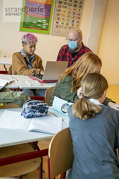 Junge Teenager arbeiten mit Hilfe ihres Lehrers an ihrem Laptop
