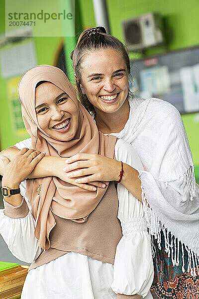 Ein lächelndes Porträt einer jungen muslimischen Frau und ihrer Freundin vor ihrer Moschee im Süden Thailands