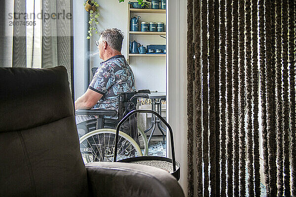 Mann im Rollstuhl denkt über das Leben nach  während er auf seinem Balkon sitzt und entspannt die Aussicht beobachtet