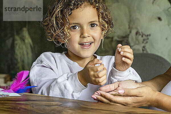 Porträt eines kleinen Jungen mit Locken  der am Tisch sitzt und mit seiner Mutter ein Spiel spielt