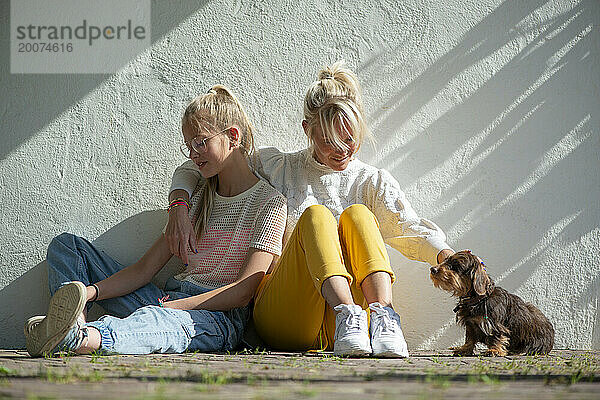 Mutter und Tochter sitzen mit ihrem Hund an der Seite des Hauses und genießen die Sonne. Glückliches und zufriedenes Miteinander