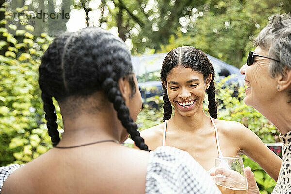 Eine reife weiße Frau plaudert und lacht mit zwei jungen schwarzen Frauen auf einer Gartenparty