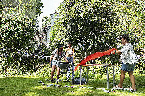 Eine Familie schmückt den Garten mit Wimpelketten und bereitet sich auf eine Grillparty vor