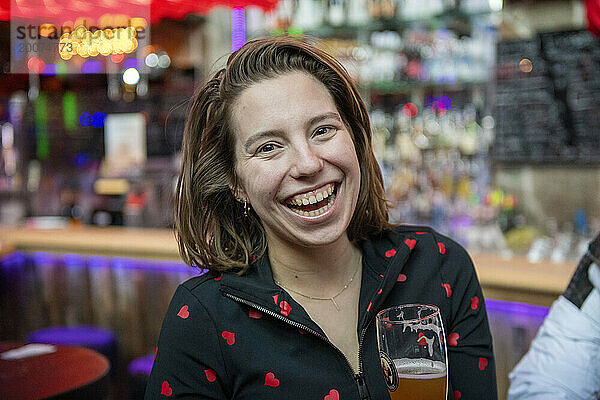 Junge Frau genießt ein alkoholisches Getränk in einer beliebten Bar. Lachen und Spaß mit Freunden haben