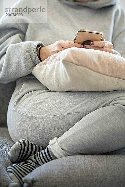 Young Woman sitting on the sofa in a clean modern home with his phone browsing
