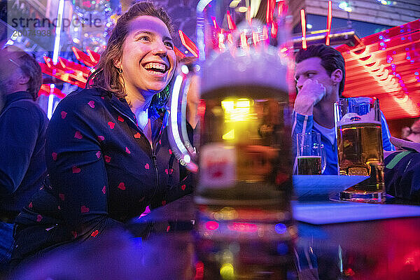 Attraktive junge Frau lacht mit Freunden in einer Bar und feiert. Alkoholische Getränke  verantwortlich