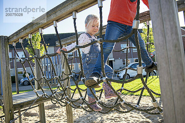 Kleines Mädchen klettert mutig durch einen Abenteuerspielplatz im öffentlichen Park