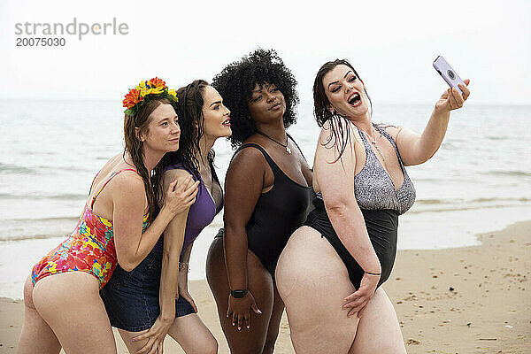 Eine gemischte Gruppe Freundinnen vergnügt sich am Strand und macht ein Selfie.