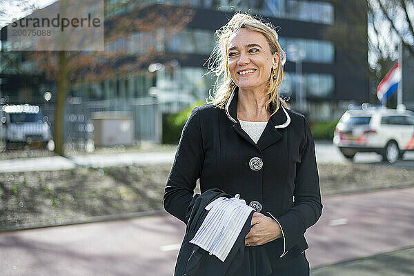 Junge berufstätige Frau steht lächelnd in der Öffentlichkeit und geht glücklich zur Arbeit