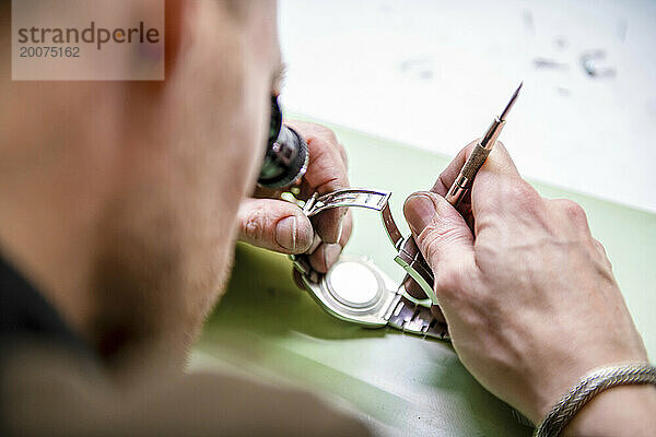 Uhrmacher repariert eine klassische Uhr  authentischer Arbeitsplatz. Verwendung eines Monokels und kleiner Werkzeuge für Reparaturen