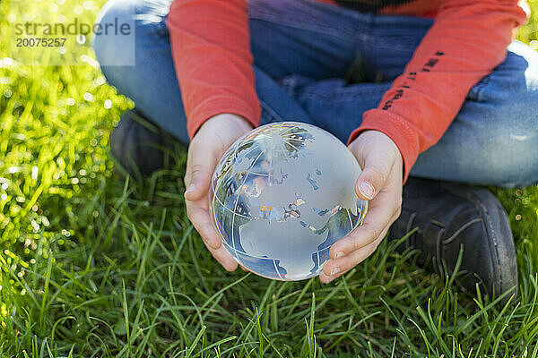 Kind hält eine Glaskugel in einem öffentlichen Park  reflektierendes Licht und klares Glas