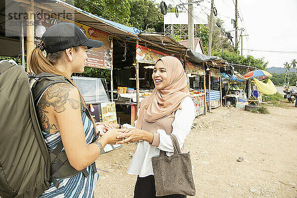 Zwei junge Frauen  eine davon trägt einen Hijab  begrüßen einander in einer ländlichen Stadt in Thailand