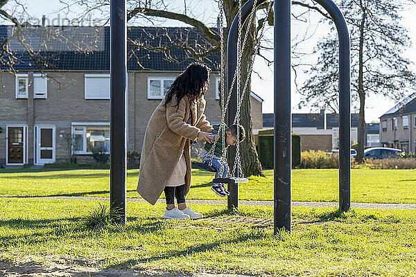 Asiatische Mutter schubst ihren Sohn auf der Schaukel