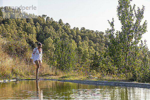 Junge attraktive Frau balanciert an einem privaten Pool entlang. Spazierengehen  entspannen und Spaß haben  während die Sonne untergeht