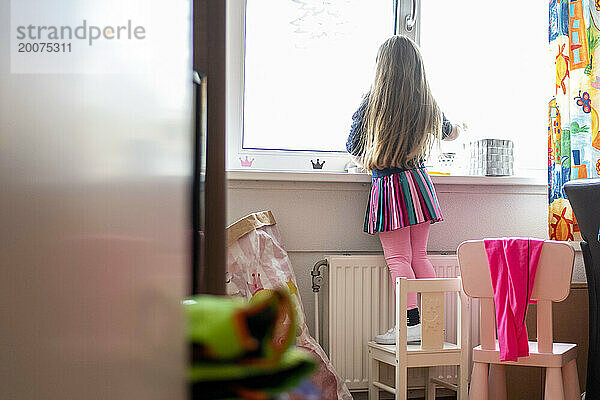 Junges Mädchen schaut aus ihrem Schlafzimmerfenster und steht auf einem Stuhl