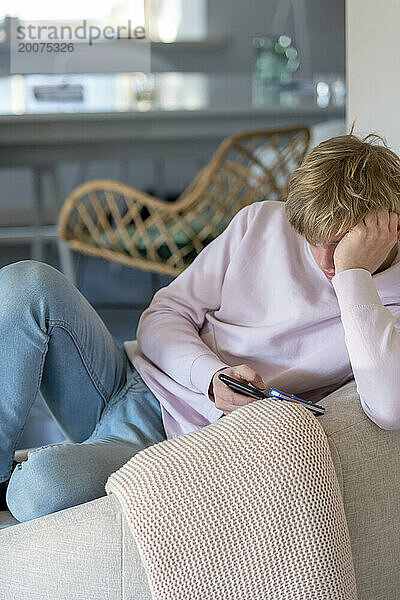 Junger Mann sitzt auf dem Sofa in einem sauberen  modernen Zuhause und surft auf seinem Telefon