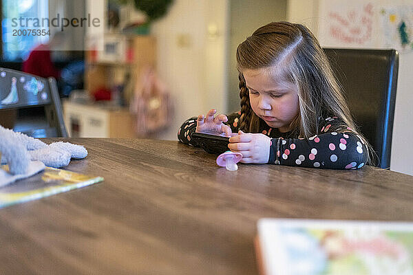 Junges Mädchen sitzt am Esstisch ihrer Familie und spielt auf dem Telefon ihrer Mutter. konzentriert versuchen zu gewinnen