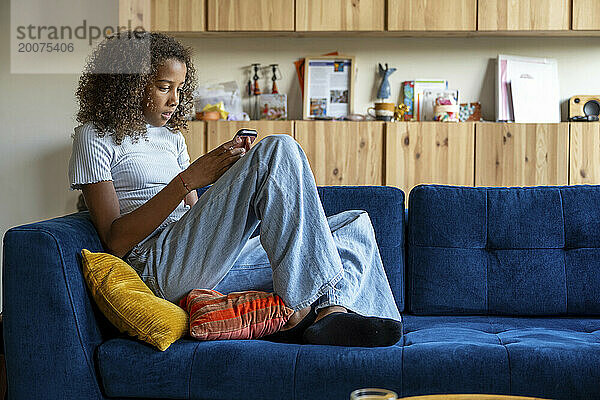 Gemischtrassiges Teenager-Mädchen sitzt auf dem Sofa und entspannt sich mit ihrem Telefon