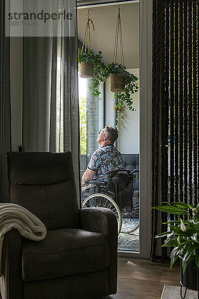 Mann im Rollstuhl denkt über das Leben nach  während er auf seinem Balkon sitzt und entspannt die Aussicht beobachtet