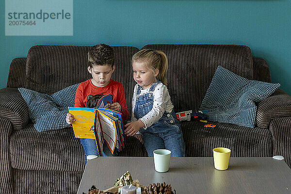 Bruder und Schwester sitzen zusammen auf dem Sofa und lesen ein Märchenbuch