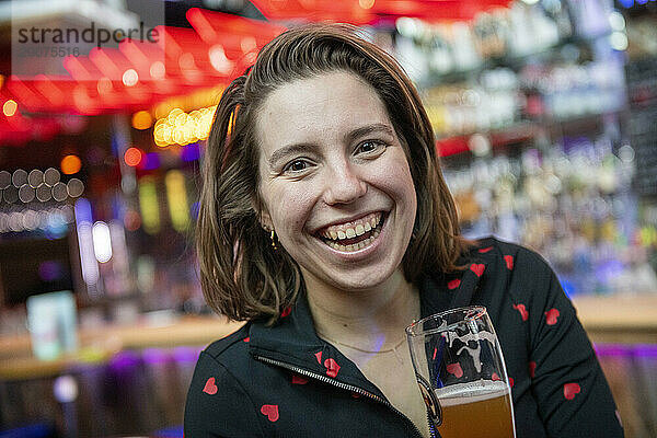 Junge Frau genießt ein alkoholisches Getränk in einer beliebten Bar. Lachen und Spaß mit Freunden haben