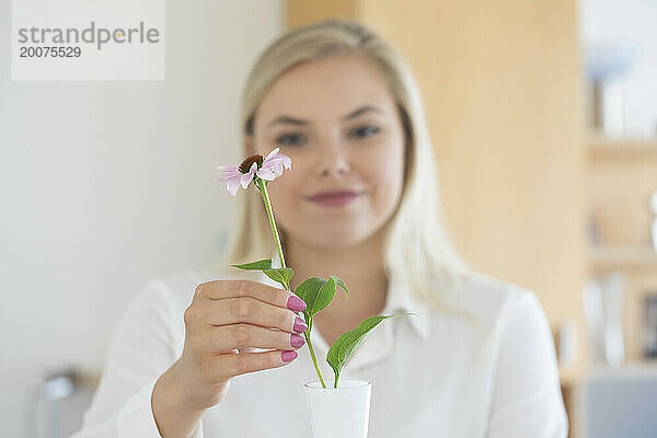 Frau mit langen blonden Haaren stellt eine Blume in eine Vase