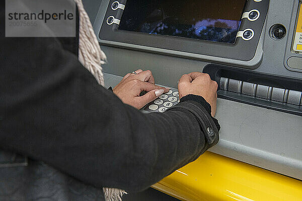 Junge Frau holt Geld aus ihrem Geldautomaten  der Geldautomat verdeckt aus Sicherheitsgründen ihre PIN