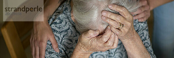 Verärgerte ältere Dame  die von ihrer Hilfe getröstet wird. Am Boden zerstört  weinend
