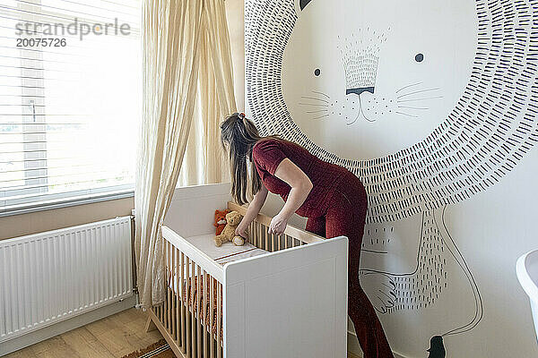 Pregnant mother arranging teddys for her new baby in its cot
