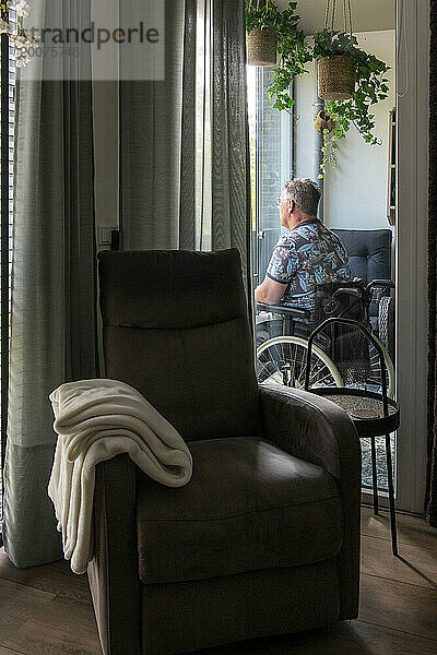 Mann im Rollstuhl denkt über das Leben nach  während er auf seinem Balkon sitzt und entspannt die Aussicht beobachtet