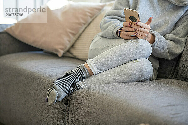 Junge Frau sitzt auf dem Sofa in einem sauberen  modernen Zuhause und surft mit seinem Telefon