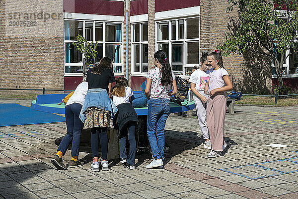 Junge Gruppe von Kindern wird von ihrem Lehrer auf dem Schulhof beaufsichtigt