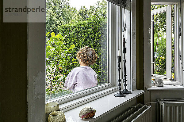 Kleiner Junge spielt im Garten durch das Fenster