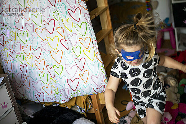 Junges Mädchen rennt mit Gesichtsmaske und Kostüm herum und spielt mit ihrer Schwester Superheldin